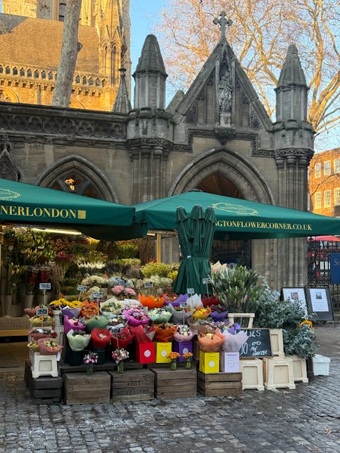 A flower stall situated outdoors in front of a historic stone building with pointed arches and decorative turrets, featuring a variety of fresh floral arrangements. The display includes bouquets with