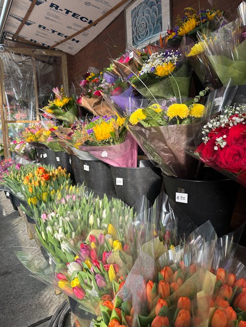 A wide view of an indoor flower shop displaying a diverse selection of fresh floral arrangements, with bouquets featuring tulips in vibrant shades of orange, pink, and white in clear wrapping at the f