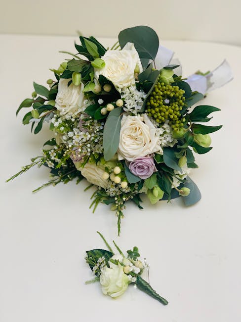 A delicate floral bouquet arranged with white roses, pale purple lisianthus, and small white filler flowers, complemented by glossy green eucalyptus and other leafy foliage. The bouquet is wrapped in